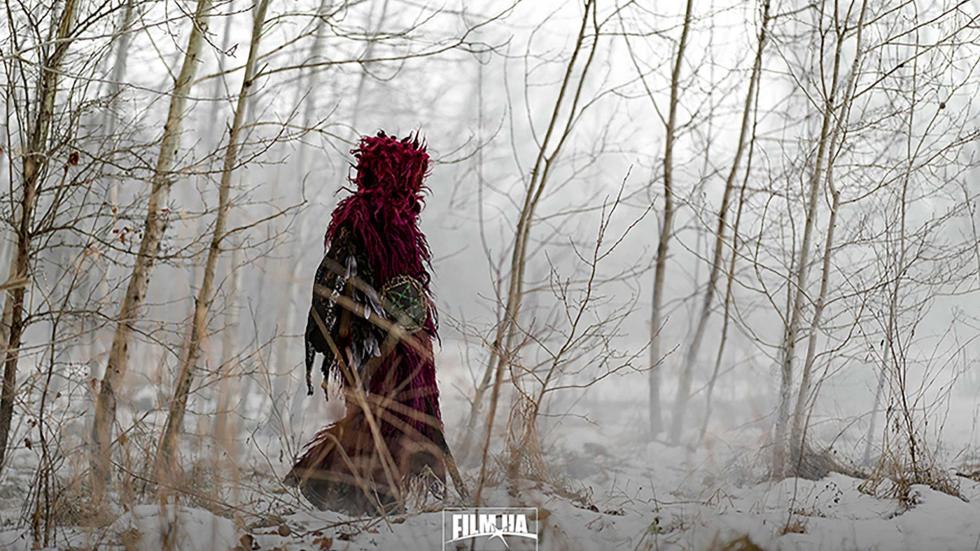 A cloaked woman walks in the foggy snow covered woods