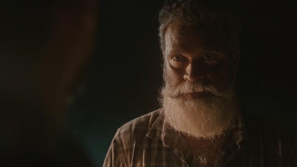 An older man with a white beard looks on