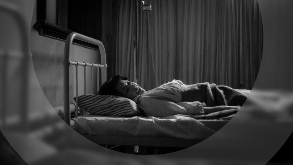 A young woman lies in bed in an asylum