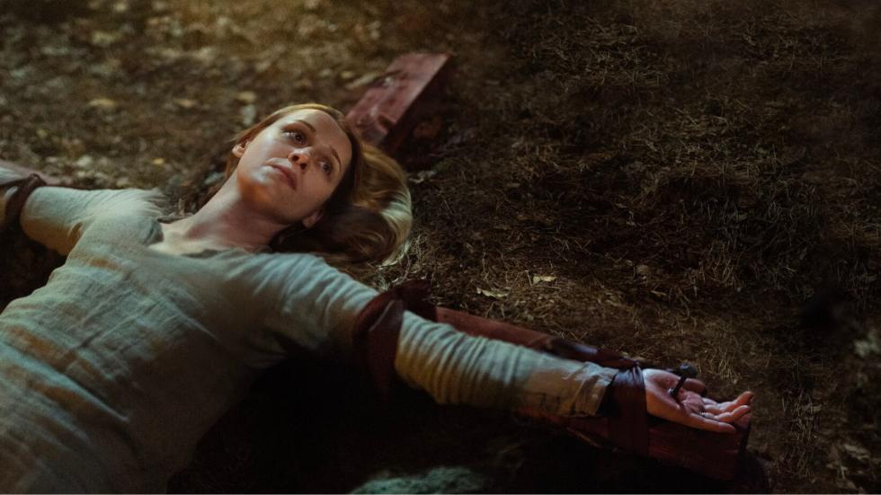 A woman is tied to a cross laying on the ground
