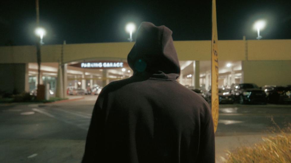Man in hoodie looks at a store from the parking lot