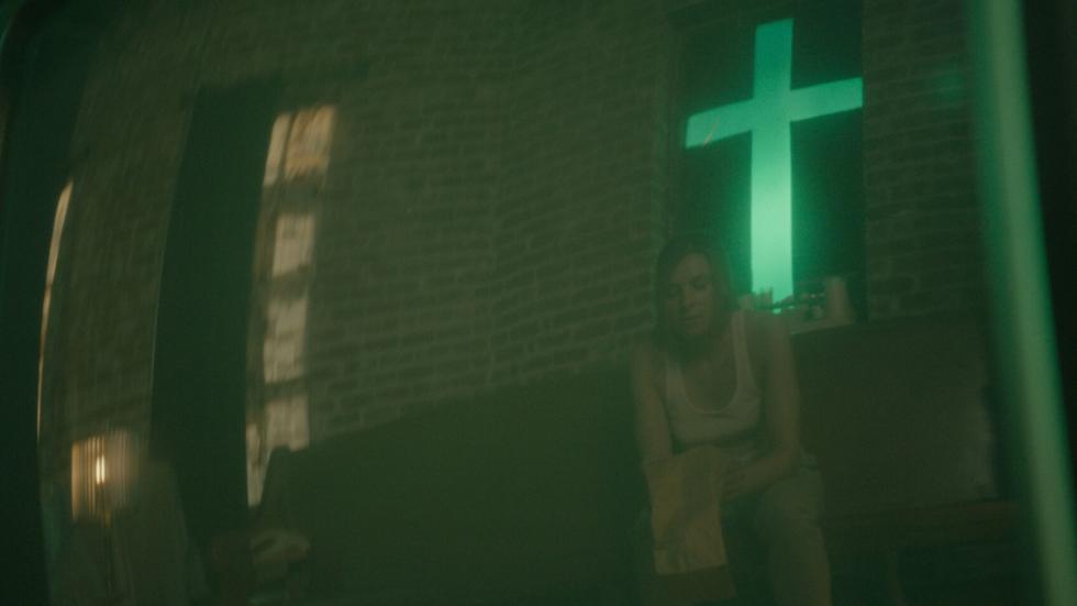 Woman sits in a church with a neon cross