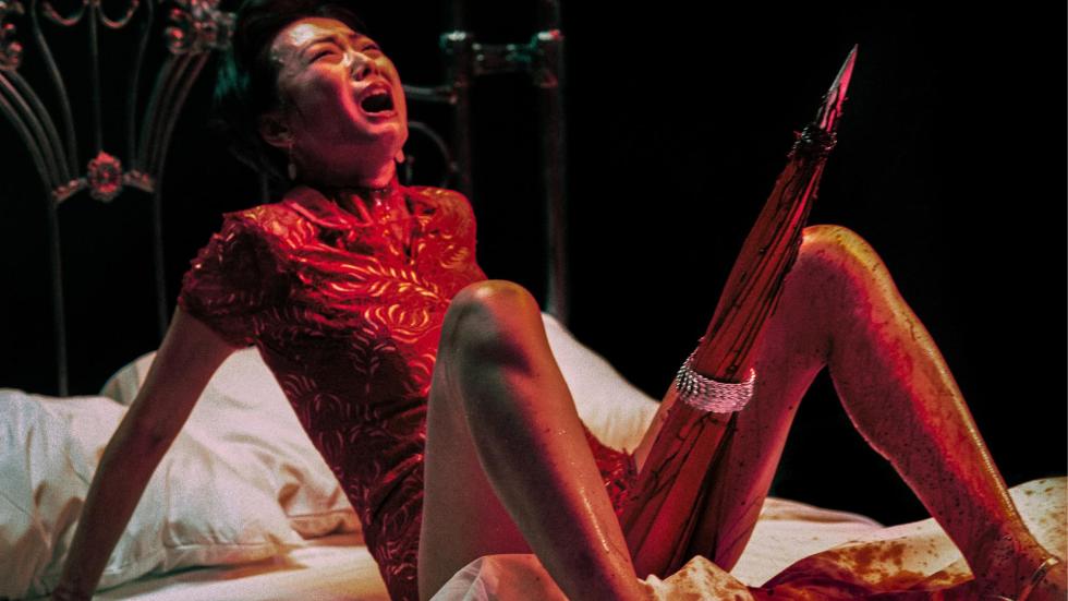 Woman on a bed with her legs open and a phallic structure emerges