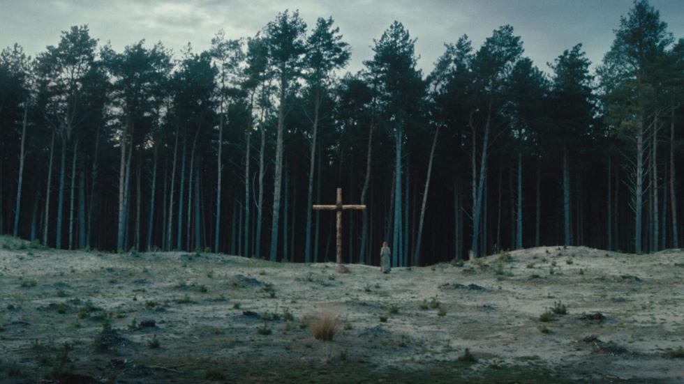 A woman walks towards the woods with a large cross planted in the ground