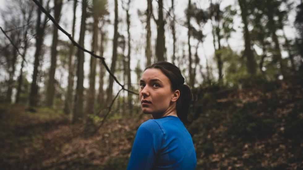 BOS Film still woman jogging through the woods stops and looks back.