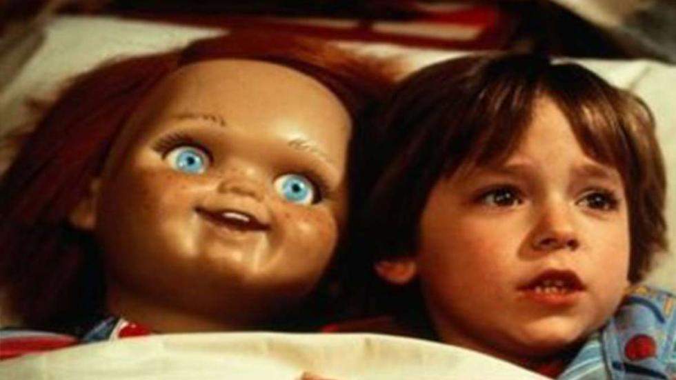 Child's Play film still boy lays in bed with Chucky doll