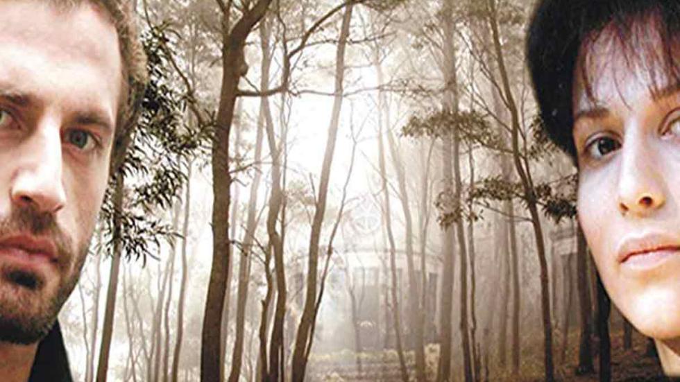 Deadline A couple in the woods with a desolated hotel shrouded in the fog behind them
