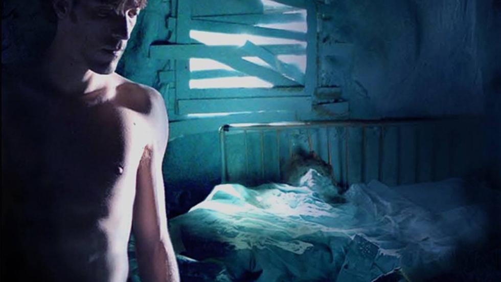 A shirtless man stands in a room with boarded up windows