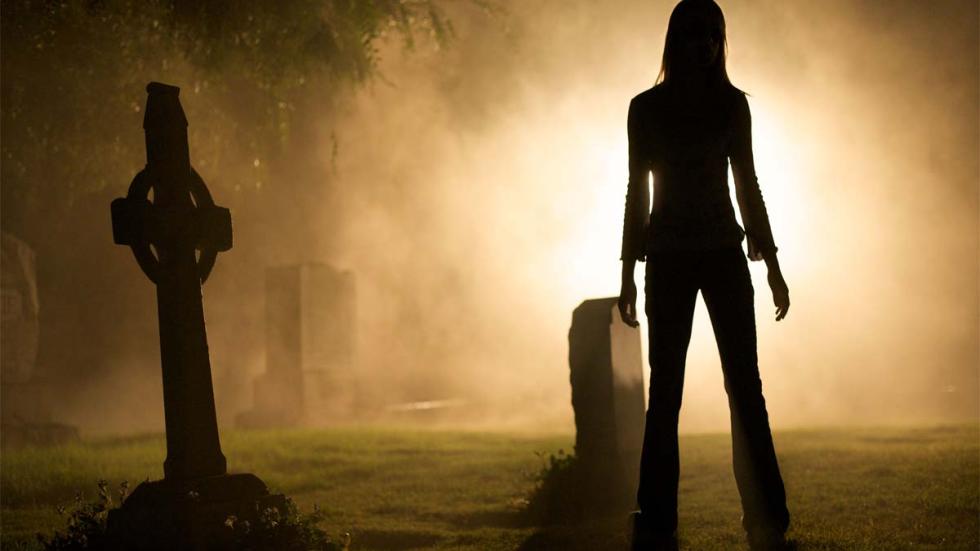 Forget Me Not woman stands in a cemetery at night
