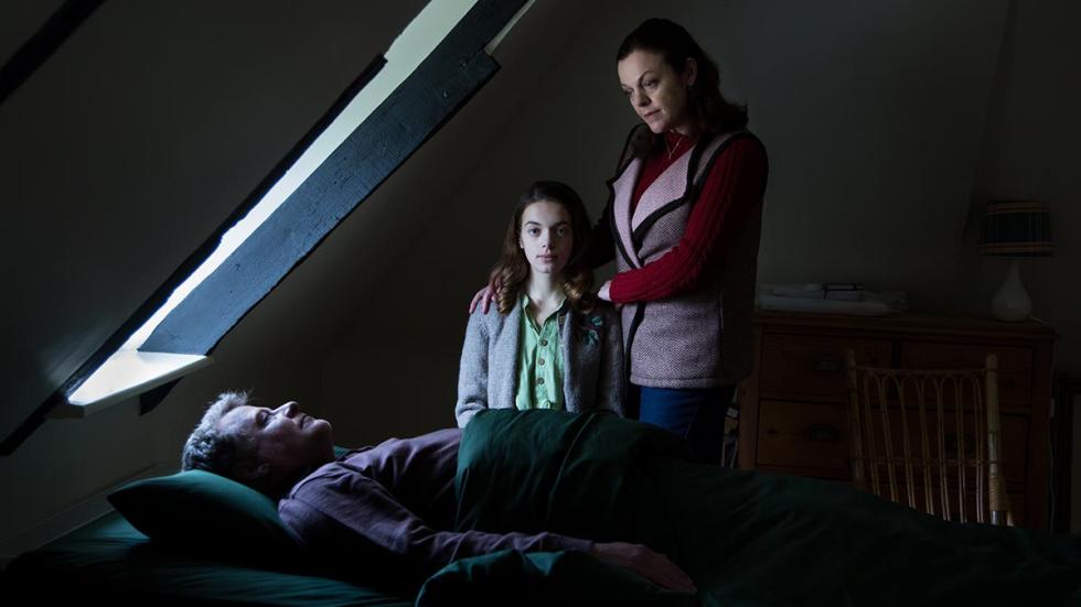 Home Education film still mother, daughter looking over father in bed