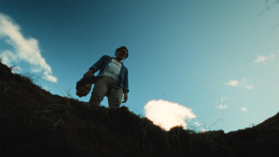 Man hold a human head above a large hole in the ground