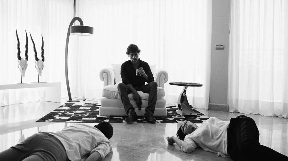MINOTAURO film still man sits on chair with dead bodies on the floor.