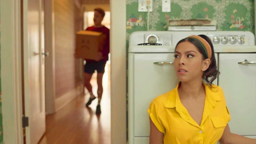 Movin Day film still woman sitting in kitchen as boyfriend brings in a moving box