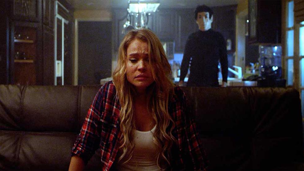 Night of the Slasher killer stands behind woman sitting on a couch