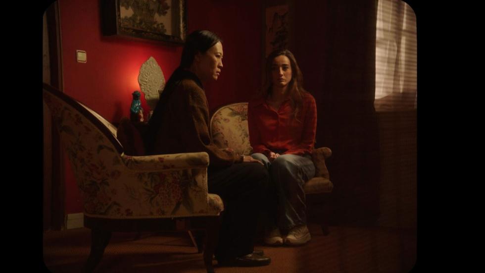 Eugenia and  Mrs. Lian sit on chairs in the living room
