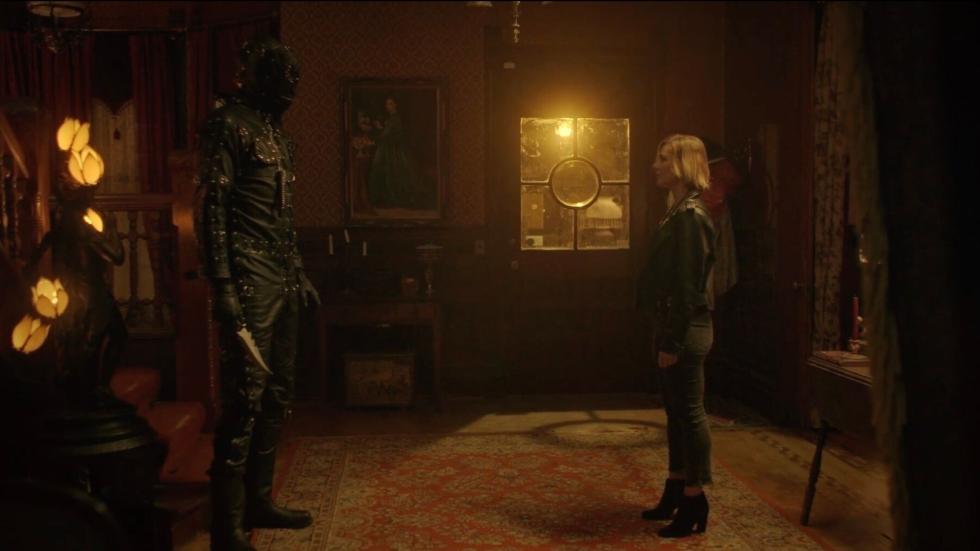 A woman faces a man in bondage attire with a knife