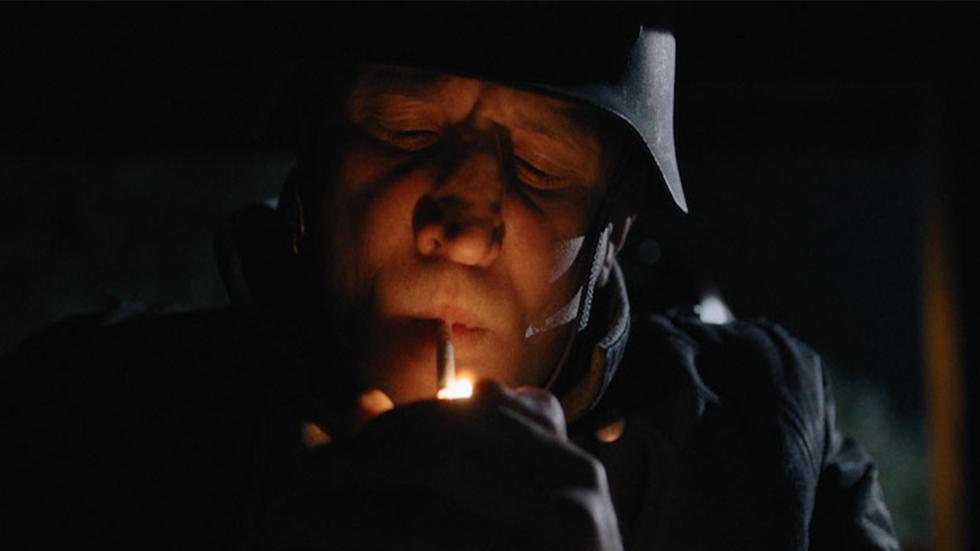 STALAG III-C film still military man lights cigarette.